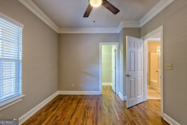 unfurnished bedroom featuring multiple windows, ornamental molding, a spacious closet, dark wood-style floors, and baseboards