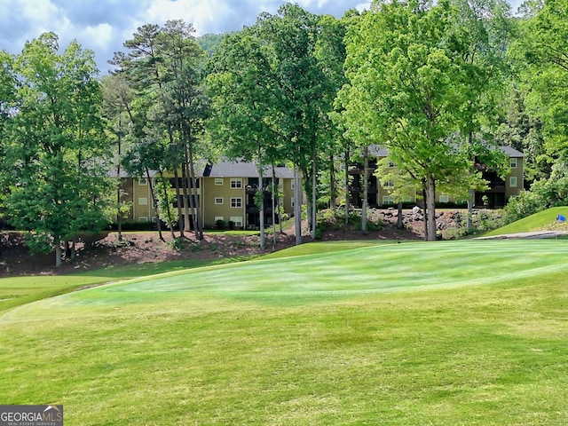 view of home's community featuring a lawn, view of golf course, and view of wooded area
