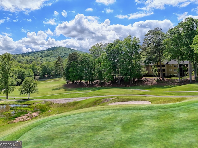 view of home's community with view of golf course, a mountain view, and a lawn