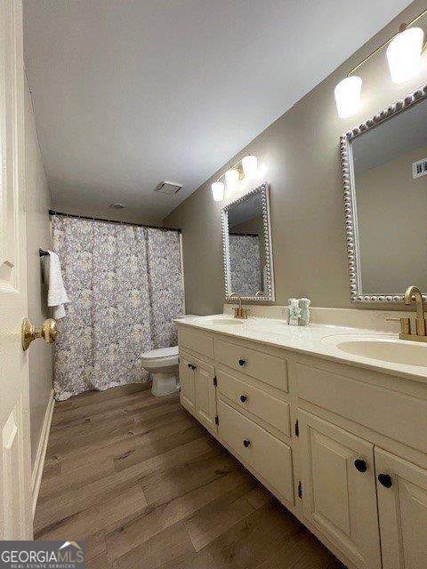 full bathroom featuring wood finished floors, toilet, and double vanity