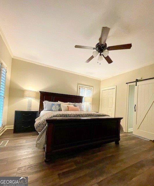 bedroom featuring ornamental molding, dark wood-style floors, a barn door, baseboards, and ceiling fan