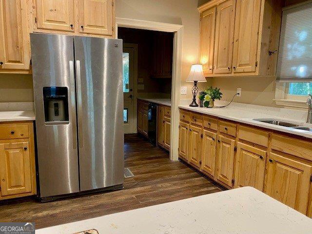 kitchen featuring stainless steel refrigerator with ice dispenser, a sink, light countertops, and dark wood-style floors