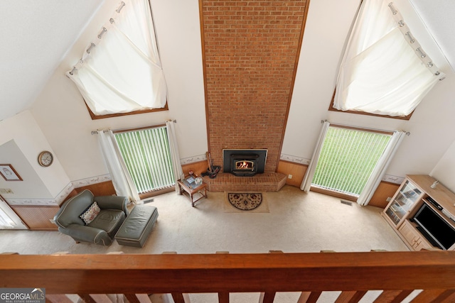 living room with a brick fireplace, a high ceiling, carpet floors, a wainscoted wall, and track lighting