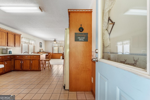 kitchen featuring brown cabinets, a peninsula, light tile patterned floors, light countertops, and a textured ceiling