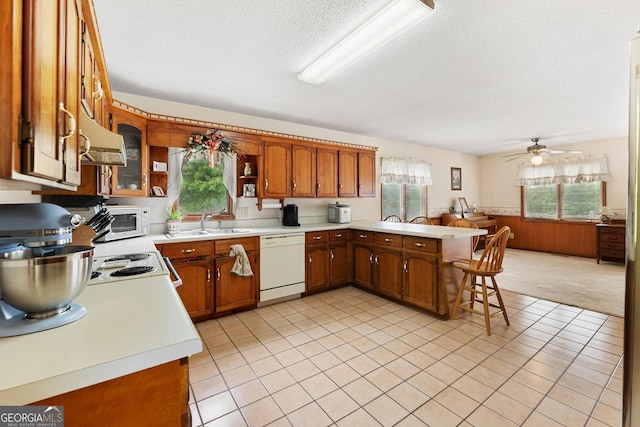 kitchen with white appliances, a textured ceiling, a wainscoted wall, light countertops, and brown cabinets