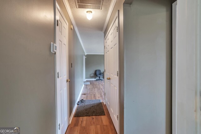 hall featuring light wood-style floors, a textured ceiling, crown molding, and baseboards
