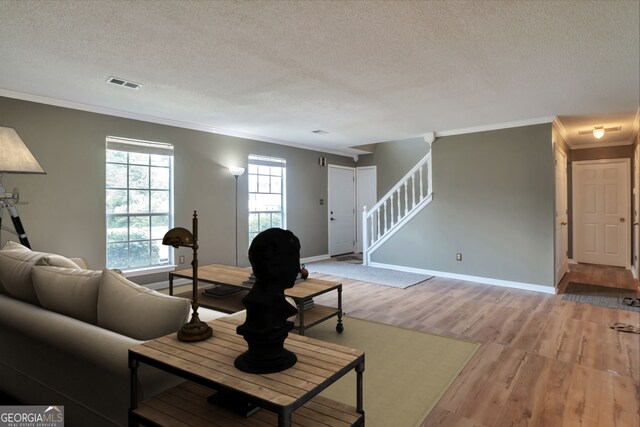 living room with crown molding, light wood finished floors, a textured ceiling, stairs, and baseboards