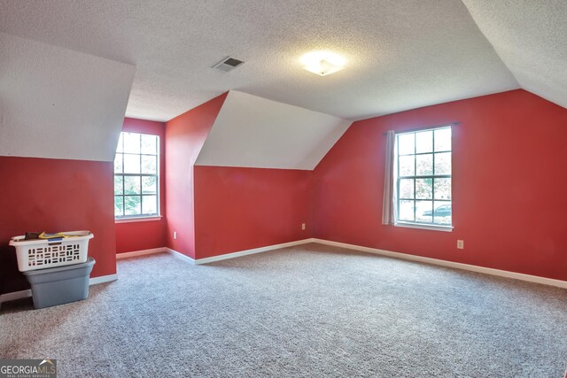 bonus room featuring vaulted ceiling, healthy amount of natural light, carpet flooring, a textured ceiling, and baseboards