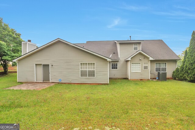 rear view of property featuring a yard, cooling unit, a shingled roof, and a chimney