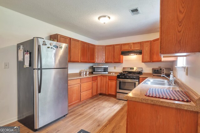 kitchen with appliances with stainless steel finishes, a sink, light wood-style floors, under cabinet range hood, and a textured ceiling
