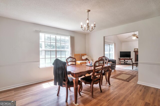 dining area featuring a chandelier, light wood-style floors, a textured ceiling, baseboards, and a ceiling fan