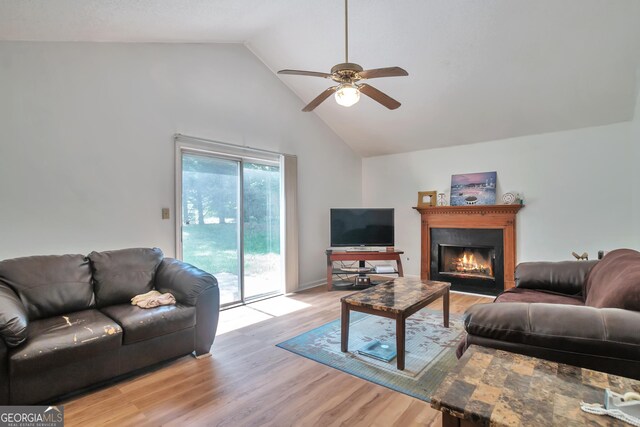 living area with a ceiling fan, high vaulted ceiling, a lit fireplace, and light wood finished floors