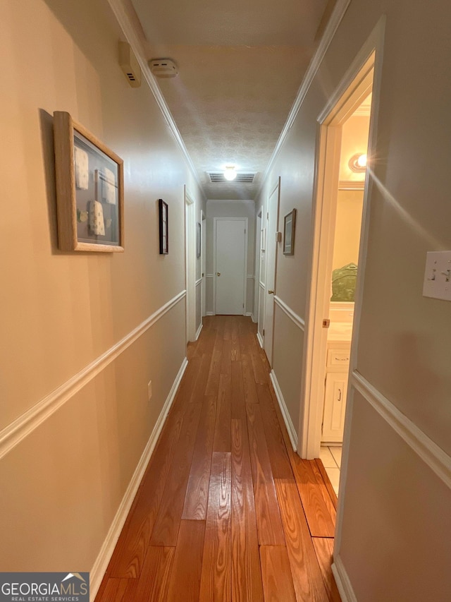 hall with light wood-style flooring, ornamental molding, and baseboards