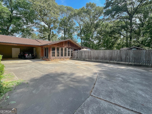 view of property exterior featuring concrete driveway, fence, board and batten siding, and an attached carport