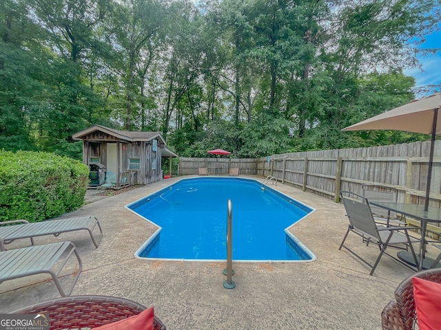 view of pool featuring a fenced backyard, a patio, an outdoor structure, and view of scattered trees