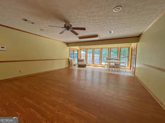 spare room with ornamental molding, wood finished floors, a ceiling fan, baseboards, and a textured ceiling