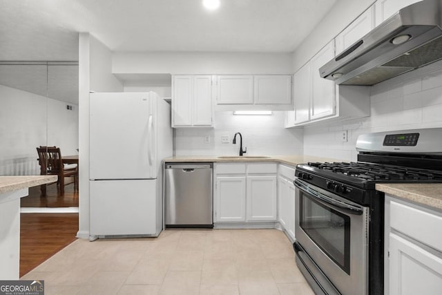kitchen with stainless steel appliances, a sink, under cabinet range hood, and white cabinets
