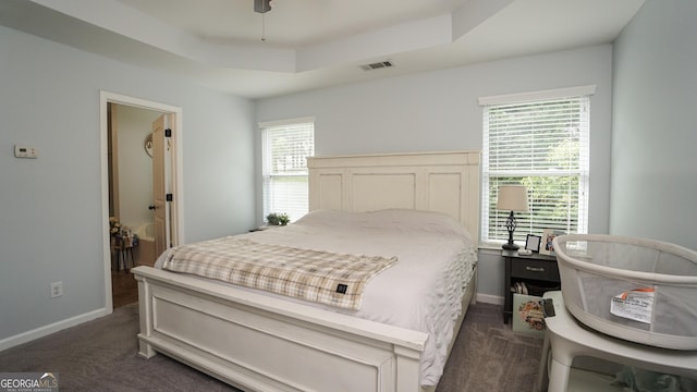 bedroom with dark carpet, a raised ceiling, and baseboards