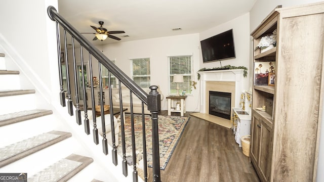staircase with ceiling fan, wood finished floors, and a fireplace