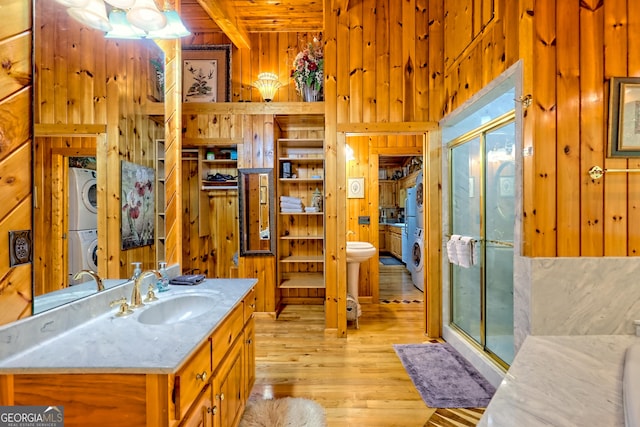 full bath with wood walls, stacked washer / drying machine, a shower stall, wood finished floors, and vanity
