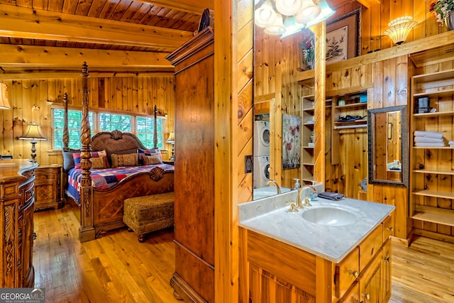 bathroom featuring stacked washing machine and dryer, wood walls, hardwood / wood-style floors, beam ceiling, and vanity