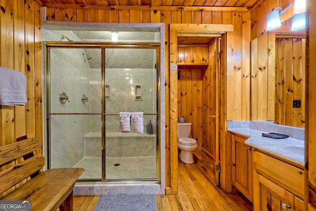 bathroom with wood finished floors, wood walls, toilet, a shower stall, and wooden ceiling
