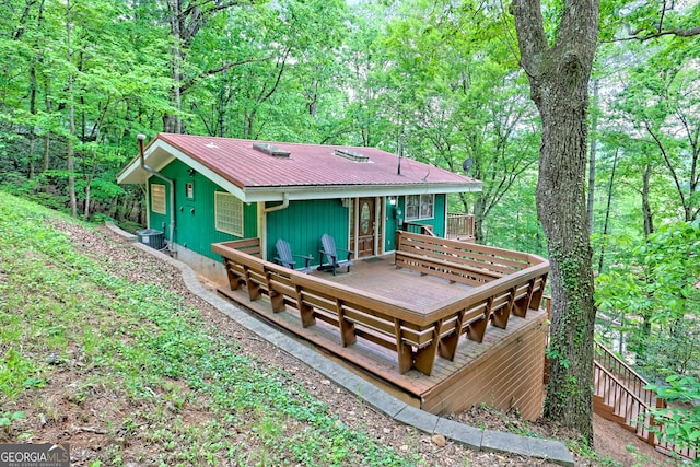 rear view of property with metal roof, a view of trees, a wooden deck, and central air condition unit