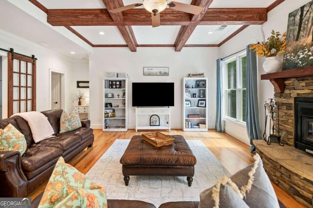 living room featuring beamed ceiling, a barn door, light wood-style flooring, a fireplace, and ceiling fan
