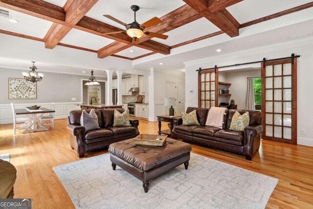 living room featuring a barn door, coffered ceiling, ceiling fan, beamed ceiling, and ornamental molding