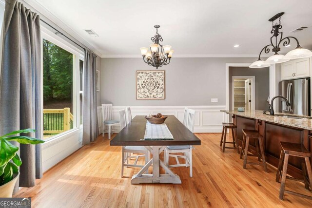dining room featuring a chandelier, ornamental molding, light wood-style floors, and a wainscoted wall