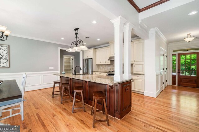 kitchen featuring a sink, light wood finished floors, appliances with stainless steel finishes, under cabinet range hood, and wainscoting