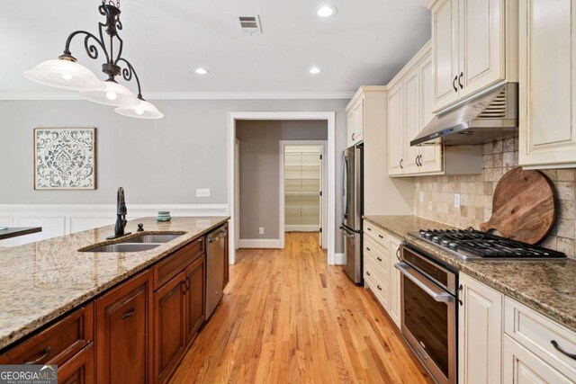 kitchen featuring under cabinet range hood, a sink, appliances with stainless steel finishes, ornamental molding, and pendant lighting