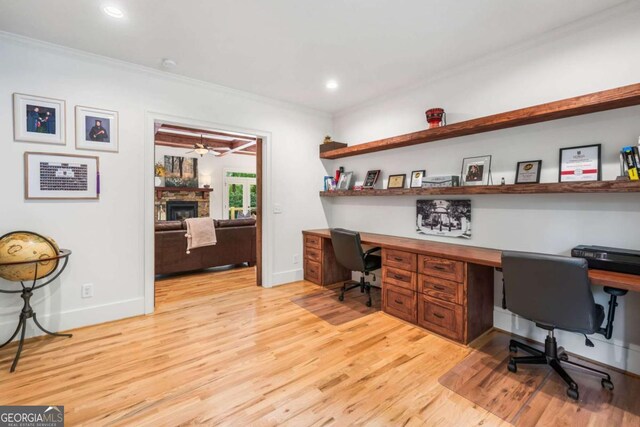 home office with crown molding, light wood finished floors, a stone fireplace, built in study area, and baseboards