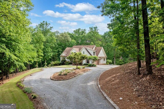 new england style home featuring curved driveway and a wooded view
