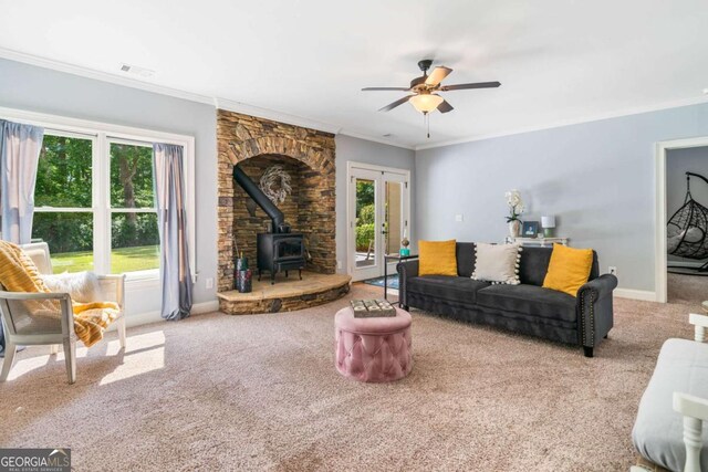 living room with french doors, a wood stove, carpet floors, crown molding, and ceiling fan