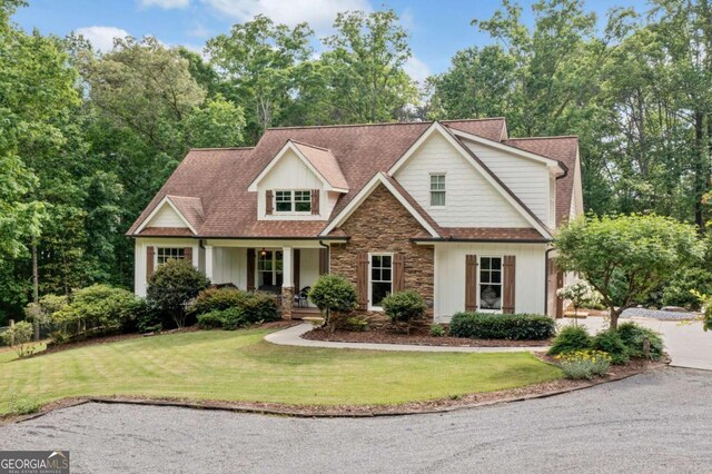 view of front of property featuring stone siding, covered porch, and a front lawn