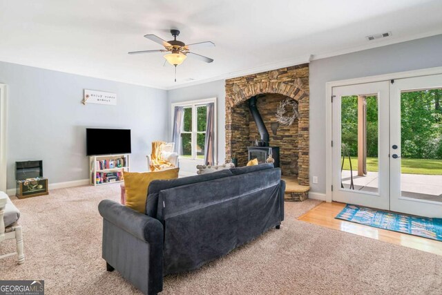 living area featuring a wood stove, french doors, a ceiling fan, crown molding, and baseboards