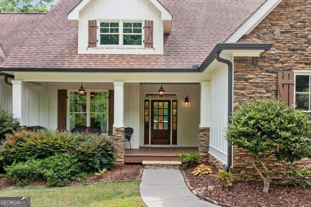 doorway to property with stone siding, board and batten siding, a shingled roof, and covered porch