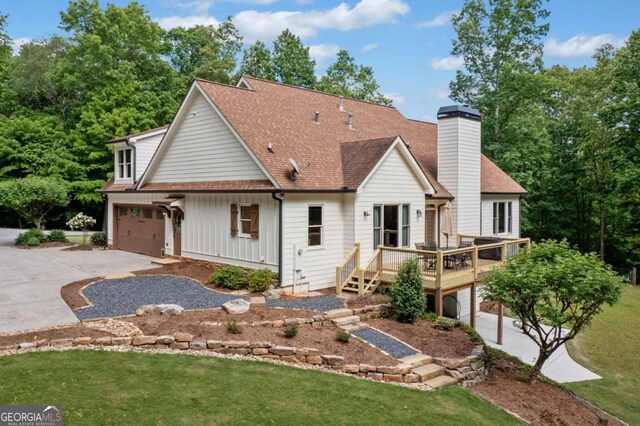 rear view of house with concrete driveway, a wooden deck, a chimney, a shingled roof, and an attached garage