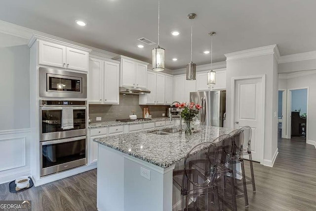 kitchen with stainless steel appliances, a sink, under cabinet range hood, dark wood finished floors, and light stone counters