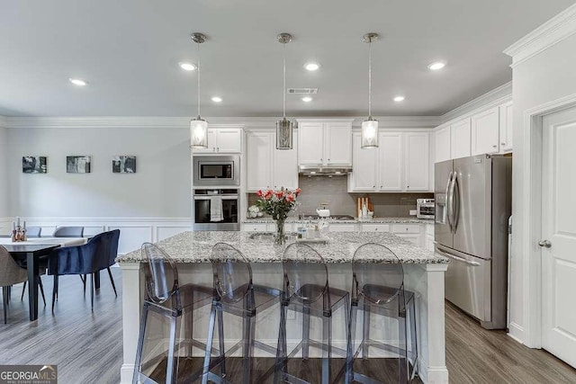 kitchen featuring stainless steel appliances, ornamental molding, under cabinet range hood, white cabinets, and a breakfast bar area