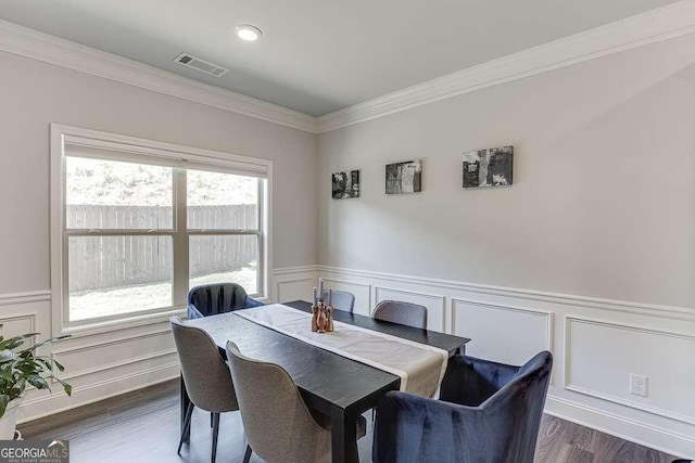 dining room with crown molding, a decorative wall, a wainscoted wall, and dark wood-type flooring