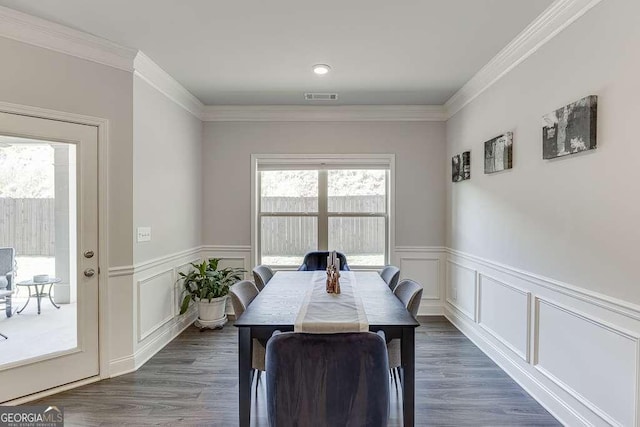 dining space featuring plenty of natural light, a wainscoted wall, crown molding, a decorative wall, and dark wood-type flooring