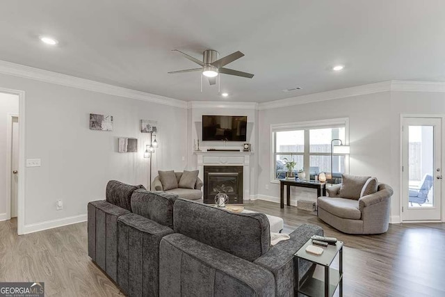 living room with ceiling fan, crown molding, baseboards, a glass covered fireplace, and wood finished floors