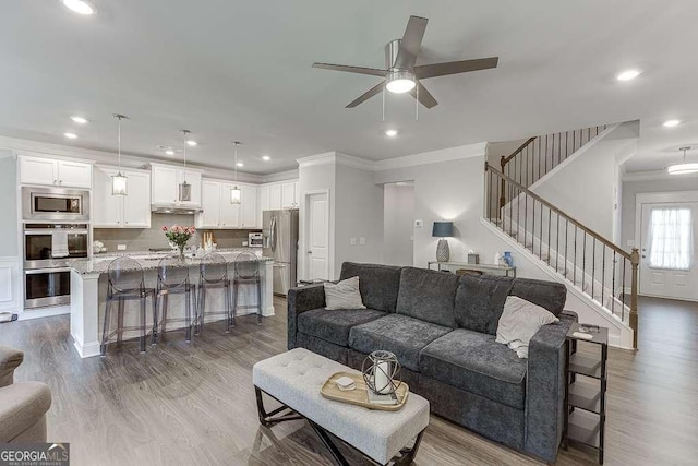 living area with crown molding, stairway, a ceiling fan, wood finished floors, and recessed lighting