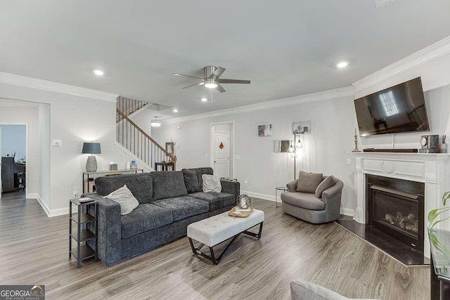 living area with stairway, wood finished floors, a fireplace with raised hearth, a ceiling fan, and baseboards