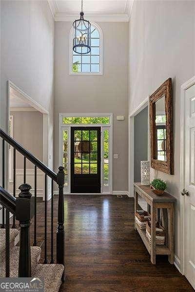 entryway with plenty of natural light, ornamental molding, wood finished floors, a chandelier, and stairway