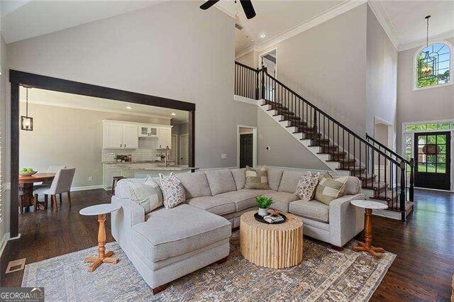 living area with a towering ceiling, dark wood-style floors, stairs, crown molding, and baseboards
