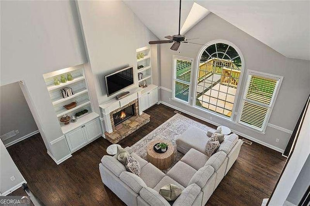 living area featuring vaulted ceiling, wood finished floors, baseboards, ceiling fan, and a glass covered fireplace