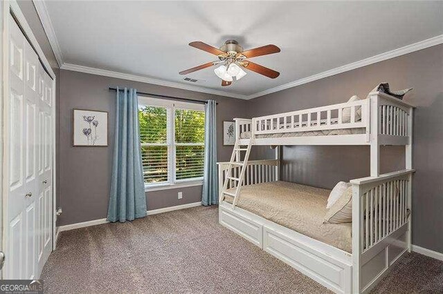 carpeted bedroom with baseboards, crown molding, ceiling fan, and a closet